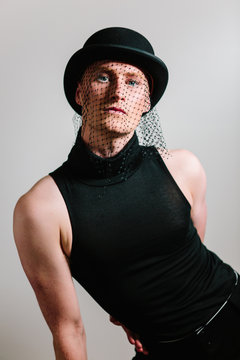 Elegant man wearing bowler hat with veil and rollneck top, cabaret style studio shoot.