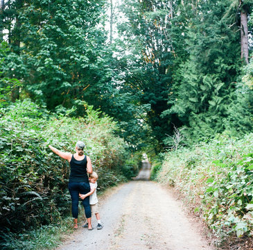 Son clings to mother's leg while she picks blackberries along a dirt road