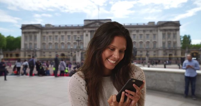 Beautiful female in grey sweater takes phone selfie while on London street, Tourist woman sightseeing in England takes picture with cell phone with landmark behind her, 4k