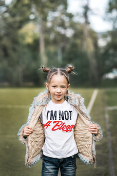 Cheeky young blond girl in a fur coat and a 'I'm not a Blogger' t-shirt standing o a football field