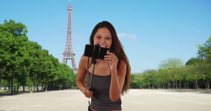Pretty tourist woman with selfie stick in Paris posing for fun photos, Vacationing millennial girl taking selfies with smartphone, making faces and pointing at Eiffel Tower, 4k