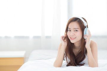 Beautiful asian young woman enjoy listen music with headphone while lying in bedroom, relax girl with earphone internet online, leisure and technology concept.