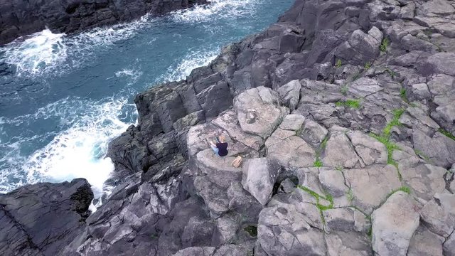 Young Lonely Woman Sitting on Volcanic Cliff by the Sea