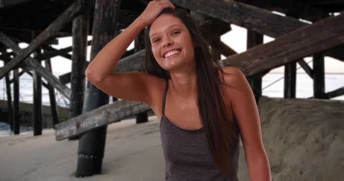 Beautiful Caucasian girl wearing striped tank top having fun at the beach, Brunette female with pretty hair smiling and laughing under the pier, 4k
