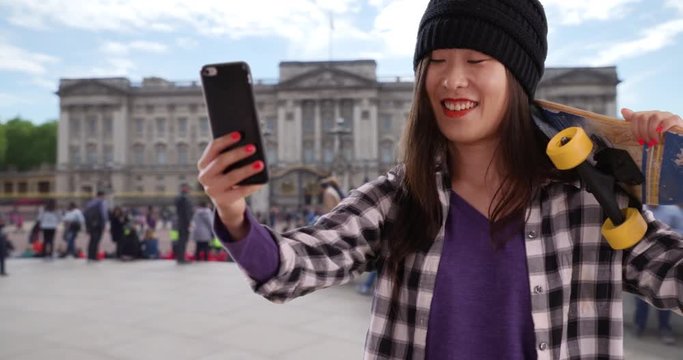 Happy hip millennial woman taking selfie with tech phone camera in London UK, Close view of young Asian woman holding skateboard in Europe, 4k