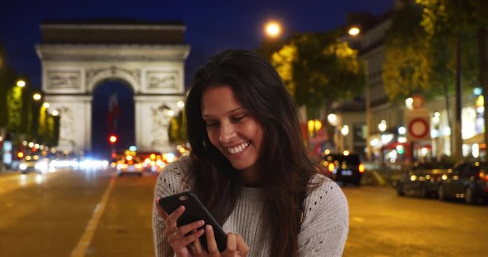 Beautiful female takes phone selfie while on urban street with Arc de Triomphe behind her, Tourist woman takes picture near Paris landmark at night to share with friends, 4k