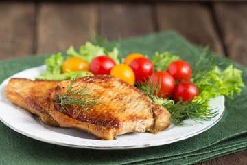 Juicy grilled pork chop with greens and tomatoes on the plate.