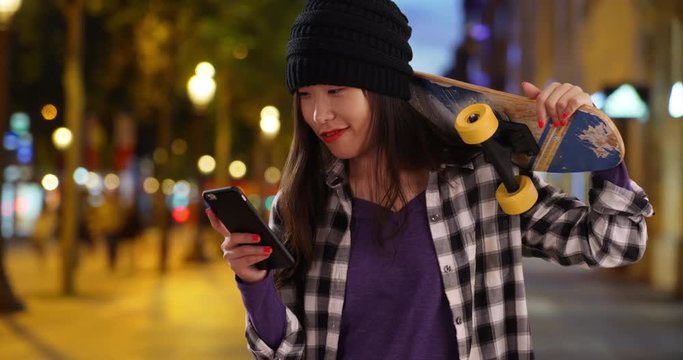 Hipster millennial woman networking on smartphone and carrying skateboard in Champs Elysees Paris France, Portrait of young Asian woman taking selfie holding a skateboard in urban setting, 4k