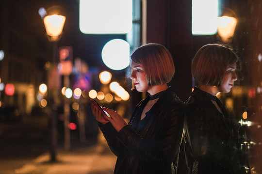 Blond woman with short hair using her smartphone on the street in the evening city.