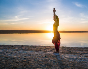 woman on the beach at sunset starts doing yoga asana training . Morning natural stretch warm-up training
