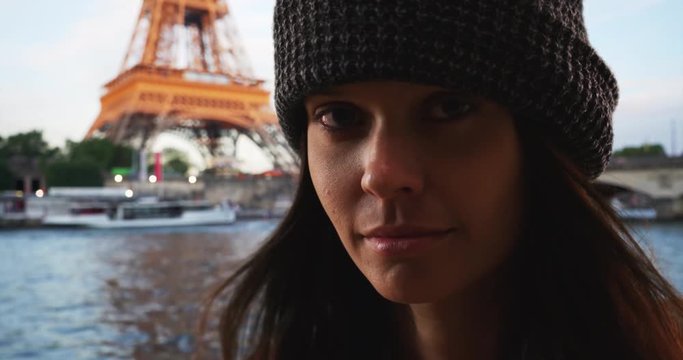 Dramatic close up portrait of woman tourist across the River Seine from the Eiffel Tower in Paris, Tight shot of Caucasian girl in her 20s looking at camera on vacation, 4k