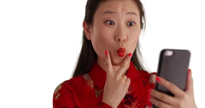 Close up of happy millennial woman smiling for selfie and wearing traditional Chinese fashion isolated on white backdrop, Young smiling Asian woman using smartphone to take selfie for copyspace, 4k