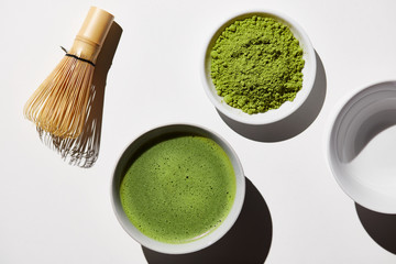 Matcha tea ingredient and bowl of prepared tea with bamboo whisk