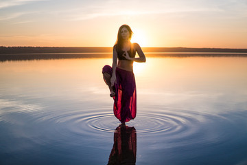 Silhouette woman on the beach at sunset standing in water. Morning natural stretch warm-up training
