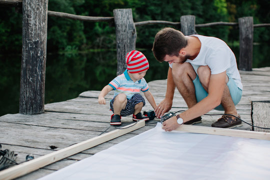 Little boy helping his father work with electric screwdriver outdoors