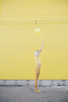 Young woman dressed in yellow standing in front of a yellow wall and holding balloon