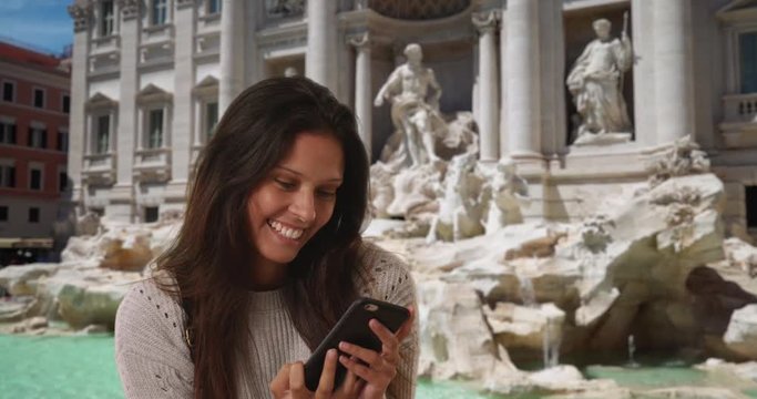 Millennial woman in grey sweater takes phone selfie in front of Trevi Fountain, Female backpacker sightsees in Rome and takes picture with cell phone to share with friends, 4k