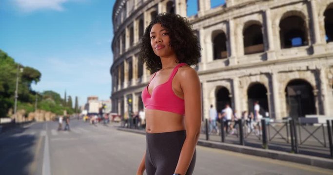 Black female jogger on urban street in Rome with towel around her neck, Portrait of athlete in active wear smiling confidently at camera, Tourist staying fit while on vacation, 4k