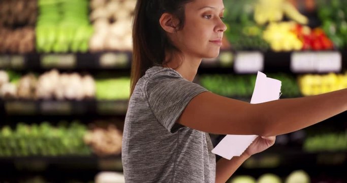 Close up of fit and healthy female customer looking through produce on shelf, Young woman with shopping list choosing best produce in supermarket, 4k 