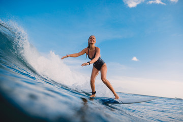 Surfer woman at surfboard on ocean wave. Woman in ocean during surfing.