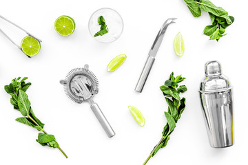 Fototapeta na wymiar Process of making mojito concept. Ingredients and crockery. Slices of lime, mint, glass with ice cubes, shaker, strainer on white background top view