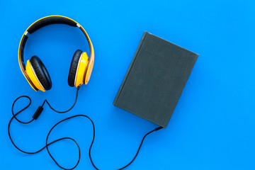 Audiobooks concept. Headphones connected with hardback book with empty cover on blue background top view copy space