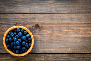 Fresh recently picked blueberries in bowl on dark wooden background top view copy space closeup