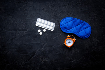Obraz premium Medicine helps get asleep. Good sleep. Sleeping pills near sleeping mask and alarm clock on black background top view copy space