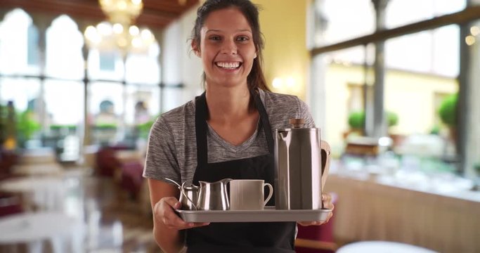 Pretty waitress in restaurant carrying tray to serve tea and coffee, Friendly server wearing apron holding tray with coffee and beverages, 4k