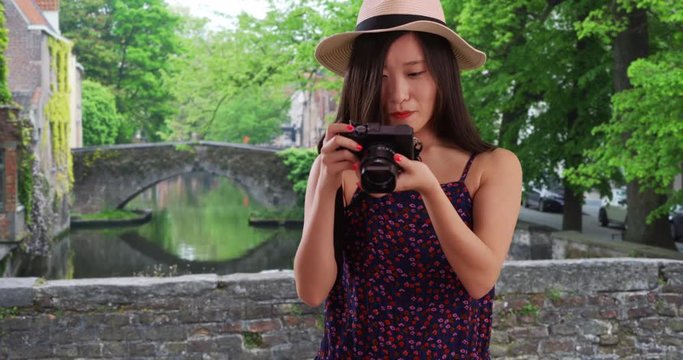 Portrait of lovely millennial photographer taking a picture with dslr camera in Bruges Belgium, Close view of young Asian woman taking a photograph over canal in Europe, 4k