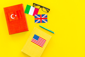 Language study concept. Textbooks or dictionaries of foreign language near flags on yellow...