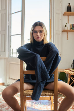 Girl in glasses and oversized pullover sitting on chair.