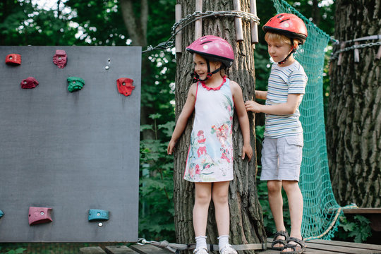 Boy and girl in helmets standing near the artificial boulder in the rope course park