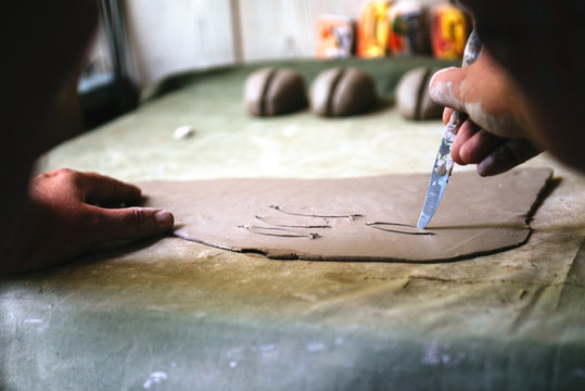 Young man working with clay and creating small ceramic objects in home studio workshop