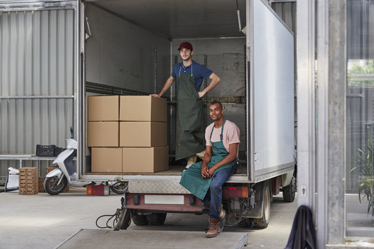 Confident Workers In Truck With Cardboard Boxes Outside Greenhouse