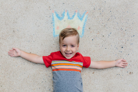 Cute happy boy laying on the ground wearing a crown drawn in chalk