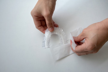 Hand opening a white package of disposable shower cap against white background