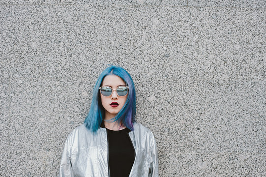 Girl with bright blue hair standing against the wall