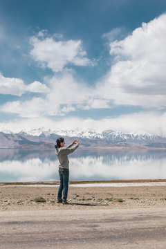female traveler taking photo of snowcovered mountain lake in tajikistan - karakol