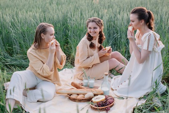 Tree lovely sisters eating melon and enjoying warm summer evening outdoors