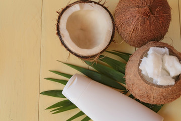 Fototapeta na wymiar Coconut oil. Natural pure coconut oil and fresh coconuts in a section on a palm leaf on a yellow wooden background. cosmetics with coconut extract. Organic Natural Cosmetics 