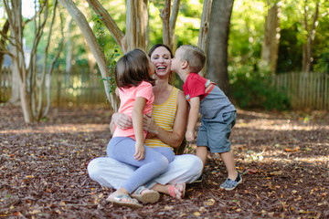 Two young children giving their mother kisses on her cheeks