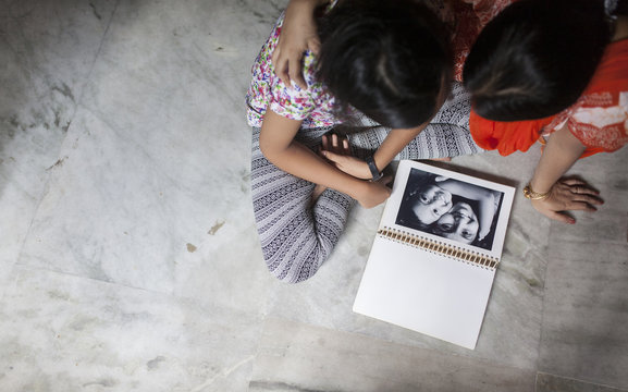 Mother and daughter looking at old photograph and making fun inside home