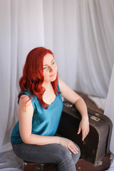 Obraz premium Travel concept: young smiling redhead caucasian woman siting on suitcase