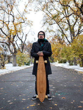 A longboarder poses in the middle of a street on a snowy autumn day