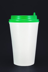 white plastic coffee cup with green lid on black background, front view with copy space