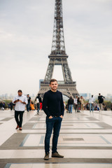 Obraz premium Handsome man wearing a dark blue pullover is standing on the background of the Eiffel Tower
