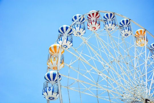 front view of half retro colorful ferris wheel at amusement park over blue sky background, copy space, vintage effect