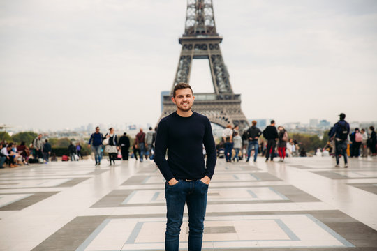 Cheerful man in dark blue pullover is standing on the background of the Eiffel Tower