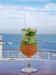 Mojito cocktail with lime and mint on a background of sea, sky with clouds. 